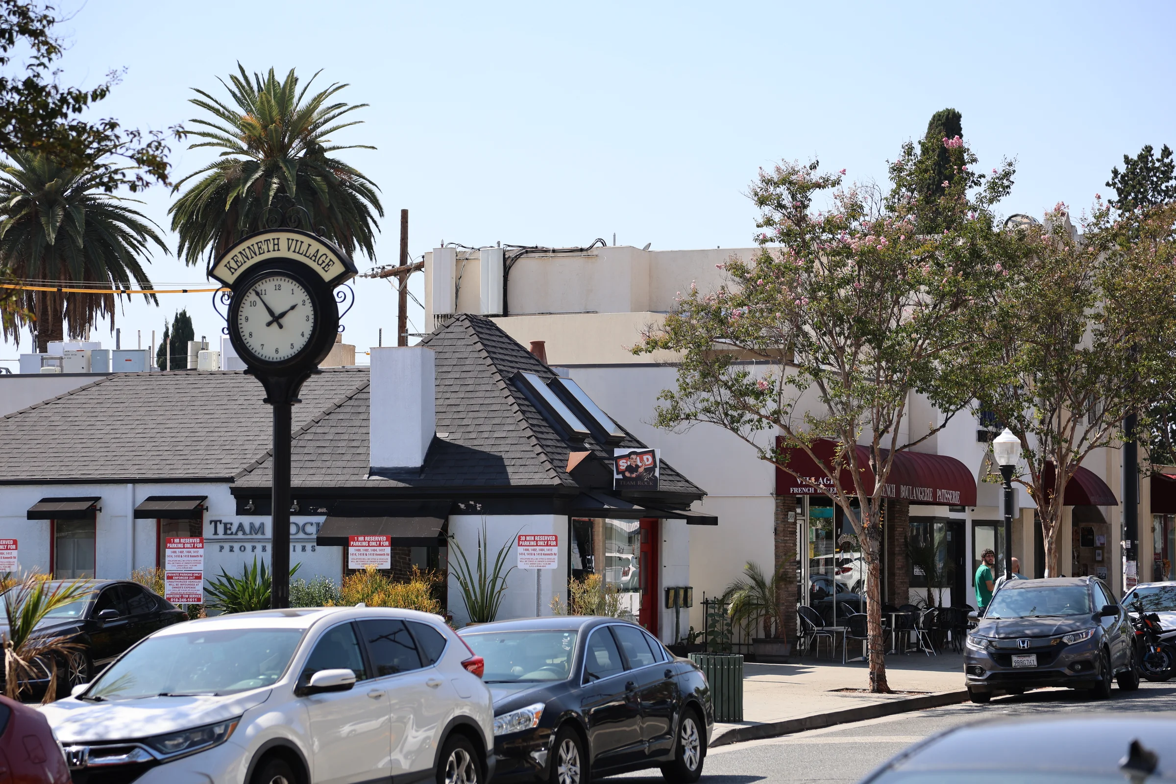 The Kenneth Village clock sign with palms and shops along Kenneth Road